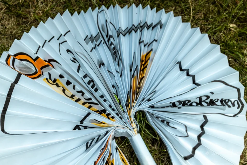 Nahaufnahme der Faecherfalten des Flipchart-Sonnenschirms mit orangefarbenen und schwarzen Marker-Details