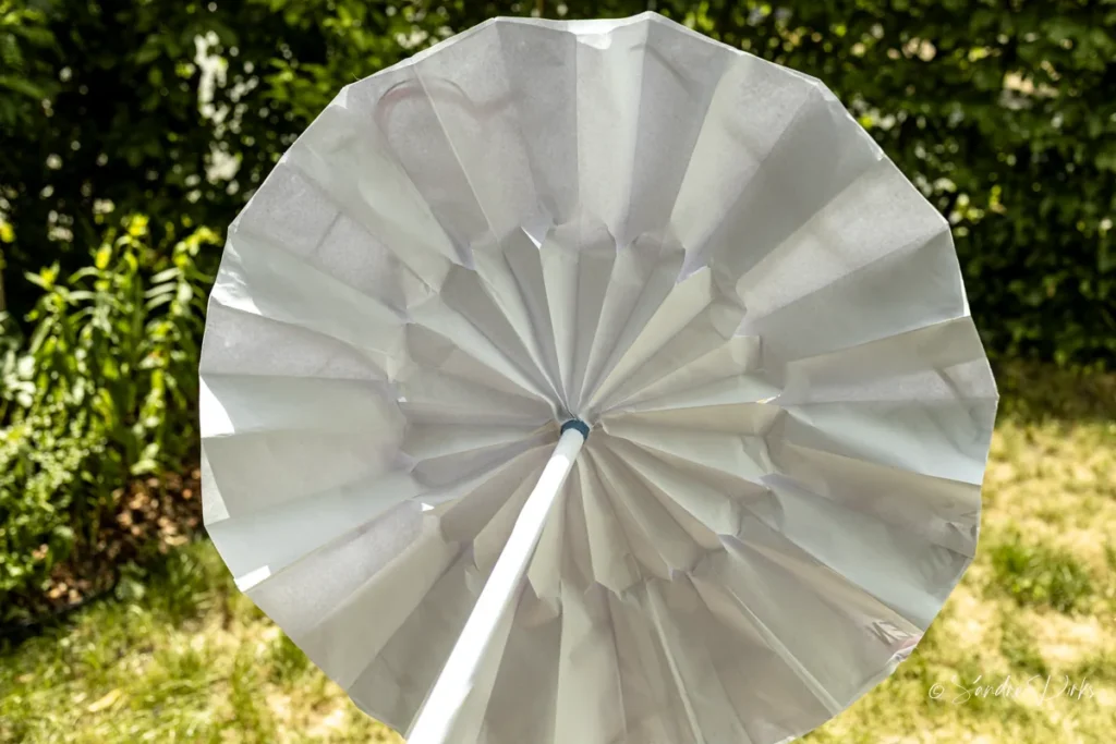 Weisser Flipchart-Sonnenschirm wie ein echter Sonnenschirm gehalten, im Hintergrund der sommerliche Garten