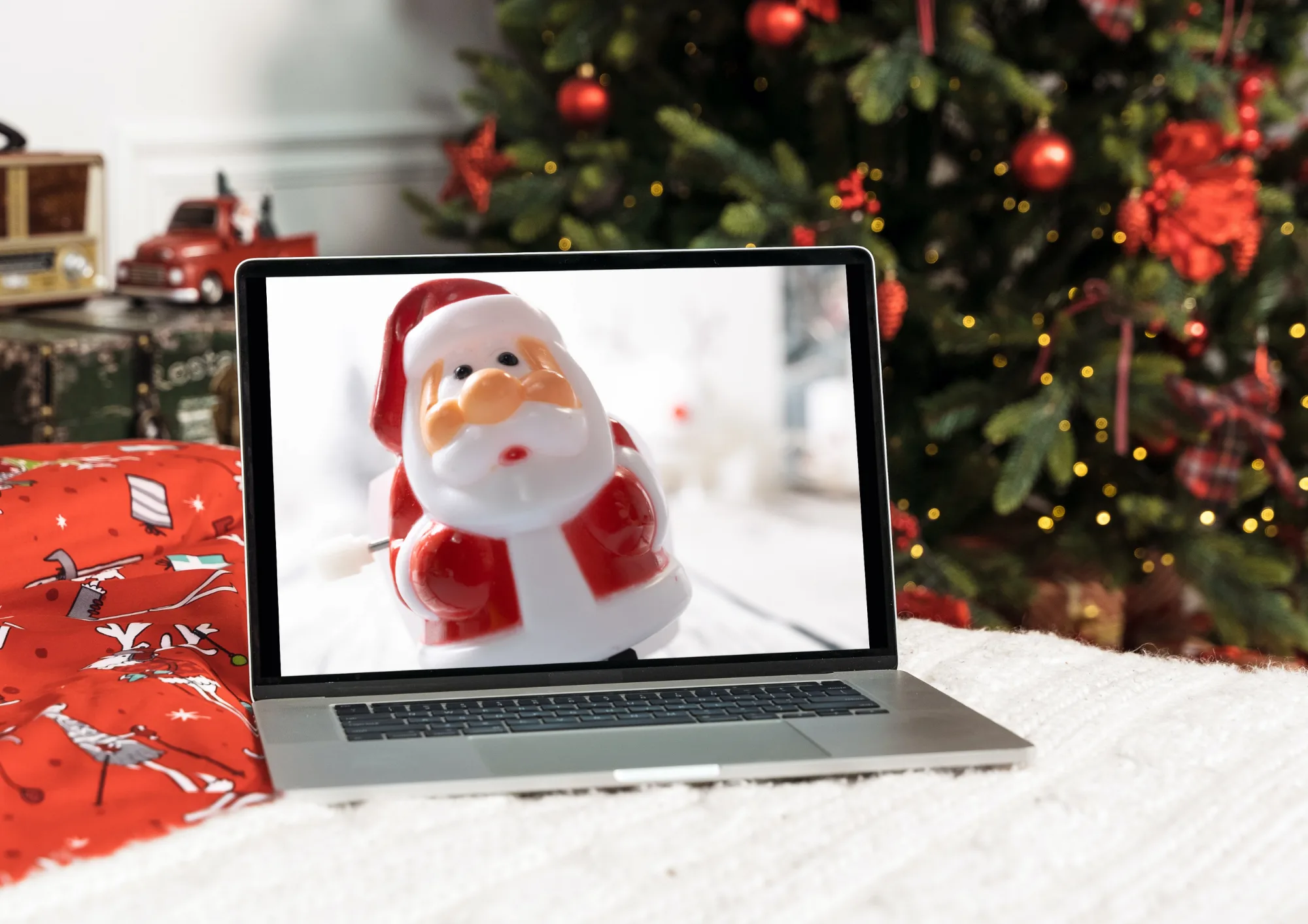 Laptop vor geschmücktem Weihnachtsbaum, auf dem Bildschirm ein aufziehbarer Spielzeug-Weihnachtsmann