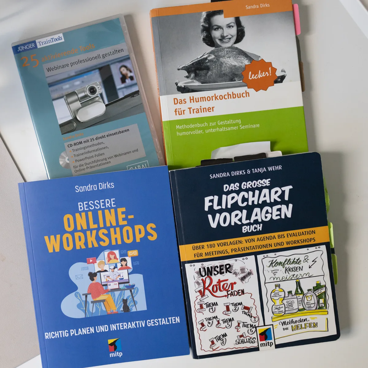 Vier Buecher von Sandra Dirks auf einem Tisch, darunter Bessere Online-Workshops und das grosse Flipchart-Vorlagen-Buch